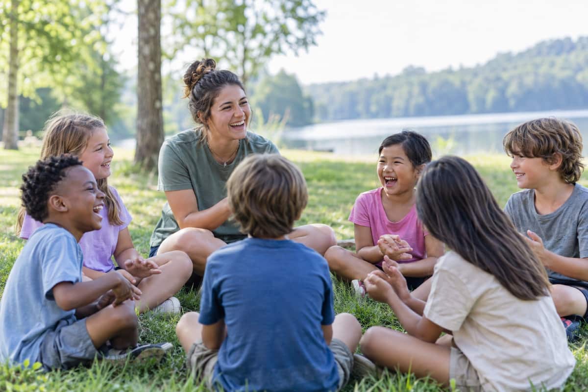 Kids laughing in a circle on the grass with a leader